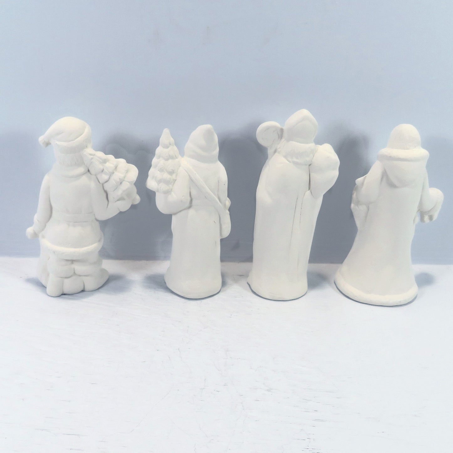 Rear view of handmade paintable santa figurines on a pale blue background