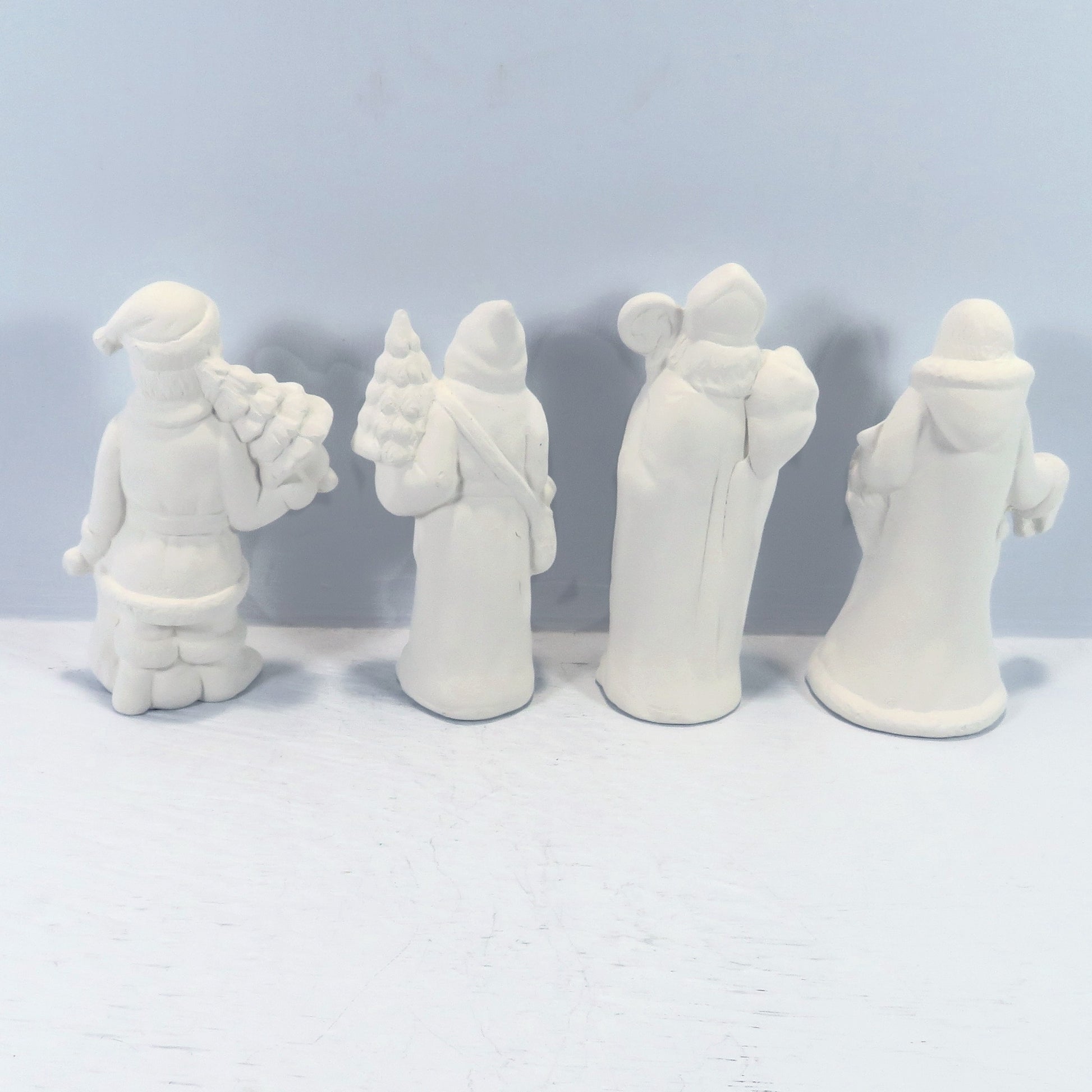Rear view of handmade paintable santa figurines on  a pale blue background