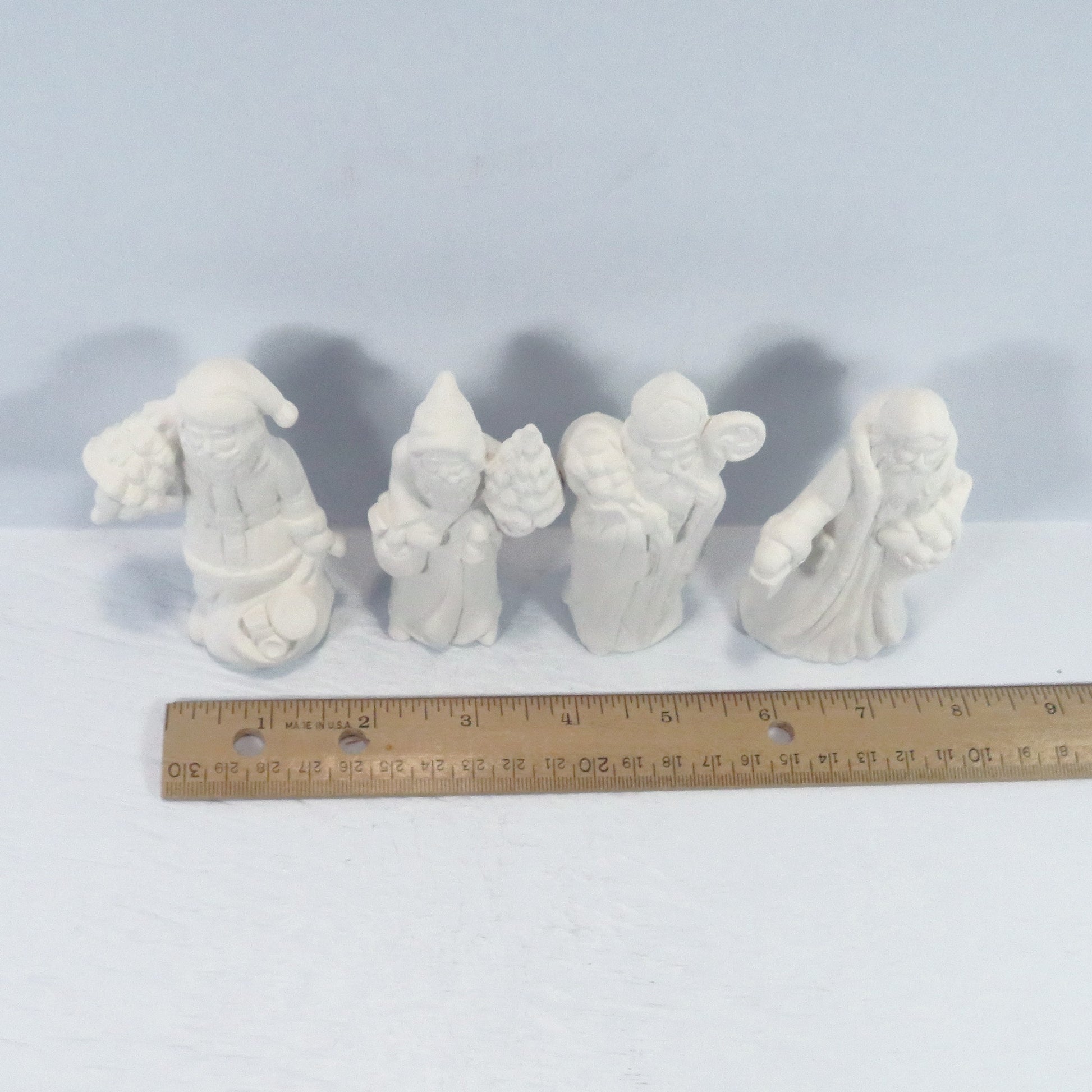 View from above of 4 handmade ceramic santa figurines near a ruler showing them to be approximately 2 inches wide.