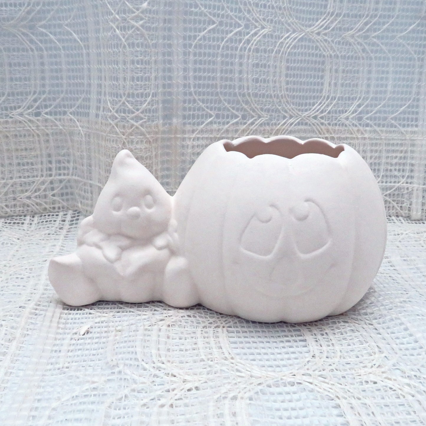 Handmade ready to paint ceramic pumpkin and ghost sitting on a table with an ecru table cloth and curtain