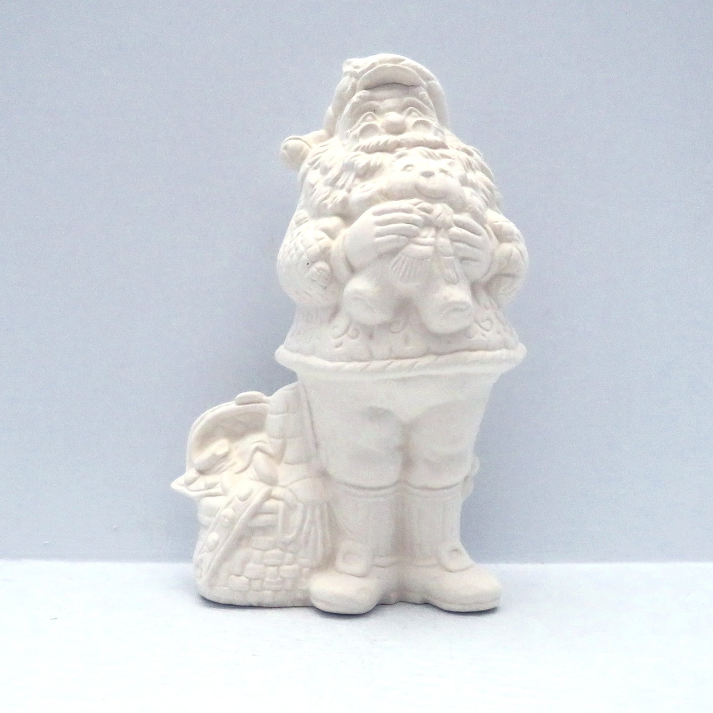 Ready to paint ceramic santa figurine standing holding a teddy bear and with a sack of toys on the floor beside him.