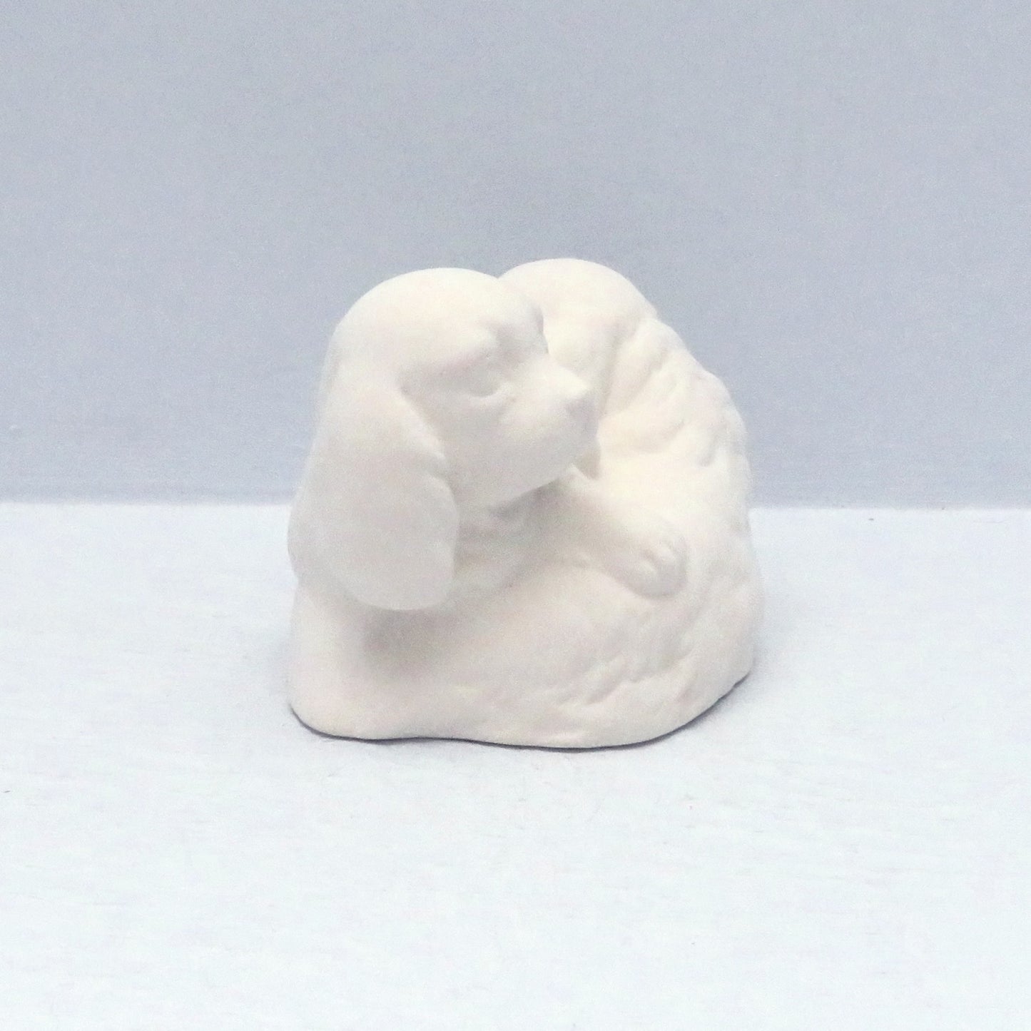 Side view of paintable ceramic puppies curled over each other on a pale blue background
