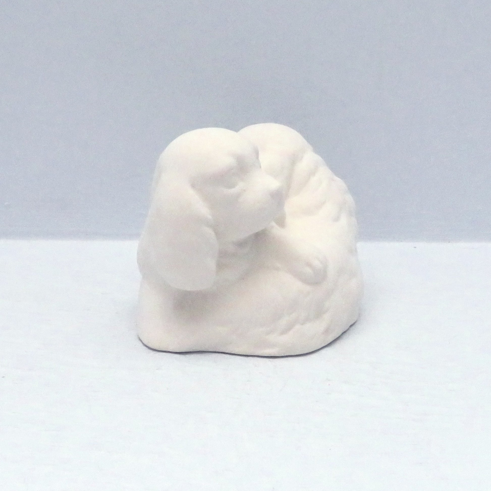 Side view of paintable ceramic puppies curled over each other on a pale blue background