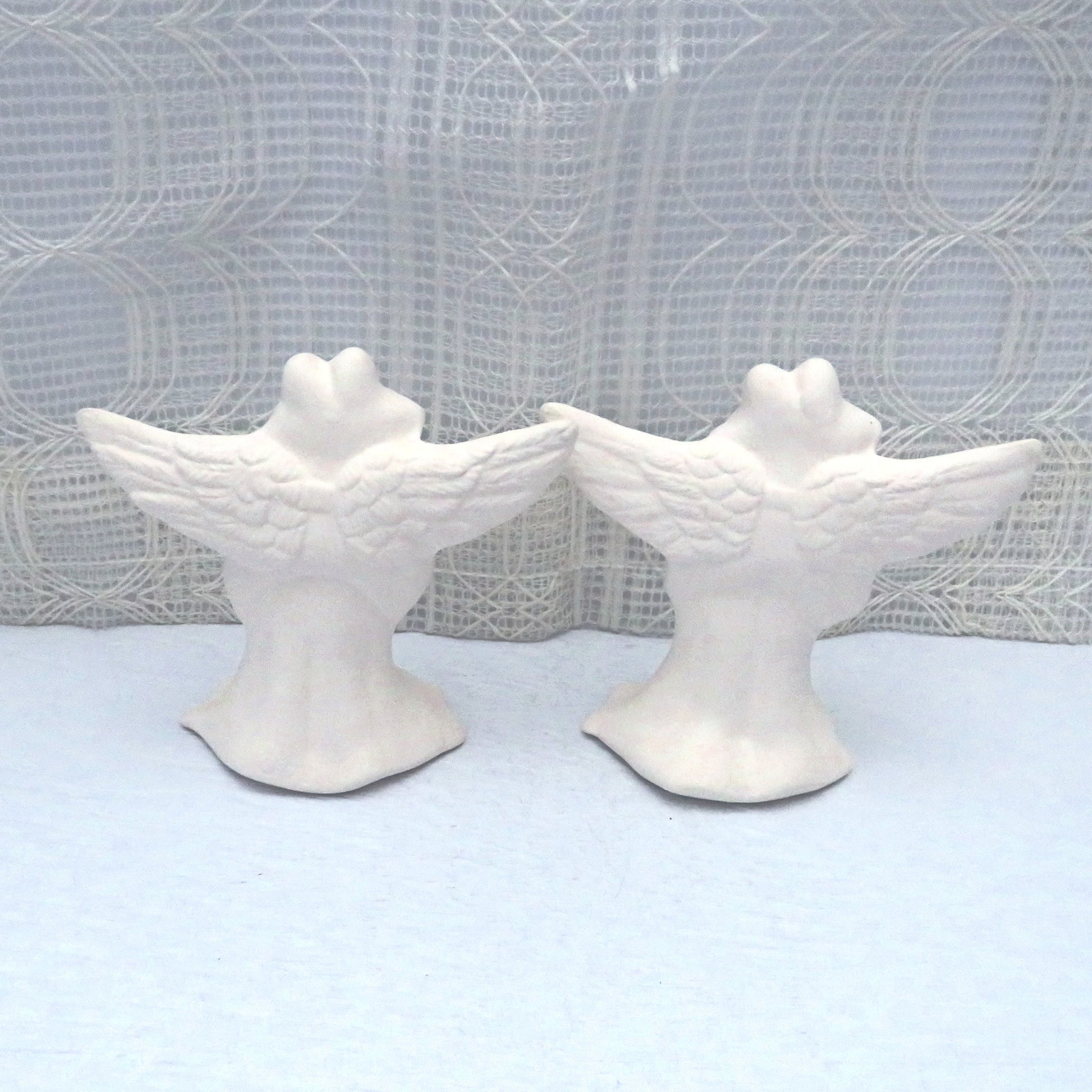 Rear view of unpainted ceramic angel frog statues.  You cann see the detail in their outstretched  wings.