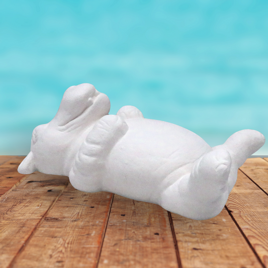 ready to paint hippo on his back with a big smile on its face.  It is lying on a rustic wooden table near the ocean.  This is a view from the side at an angle with the head slightly further away from the camera than the hips.