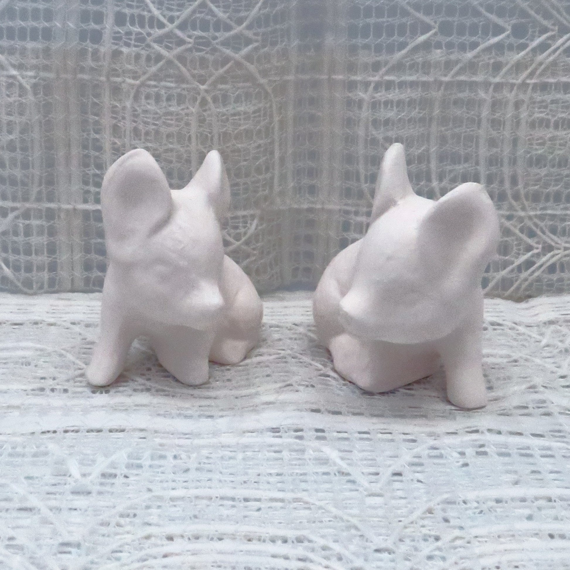 Set of 2 handmade ready to paint small pigs sitting looking toward each other.  They are sitting on a lacy background.