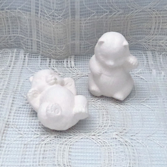 Set of 2 ready to paint ceramic panda figurines on a table with a lacey ecru cloth.  One panda is sitting and the other is lying on his back,