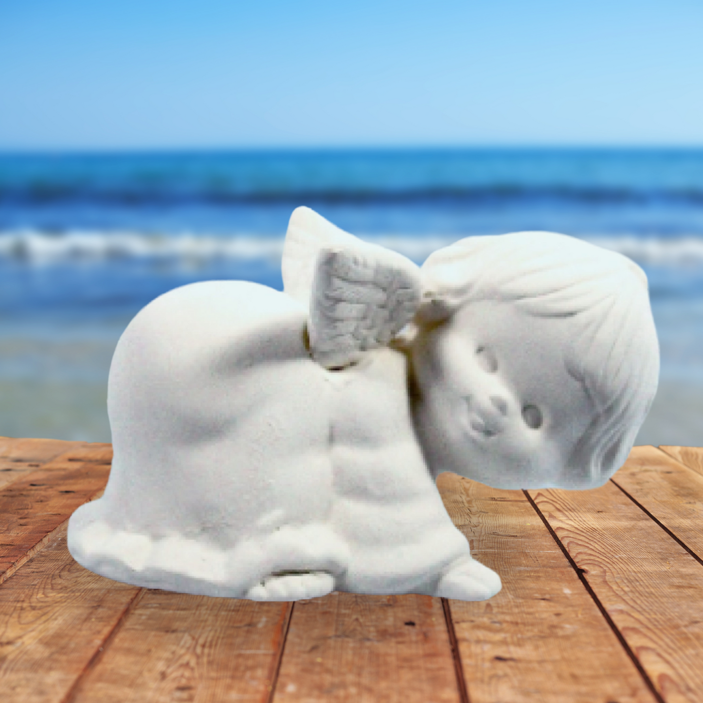 handmade ready to paint ceramic angel on all 4's with head to right.  This view shows the side of her with her face toward the camera.  She is on a brown wood tabe near the ocean.