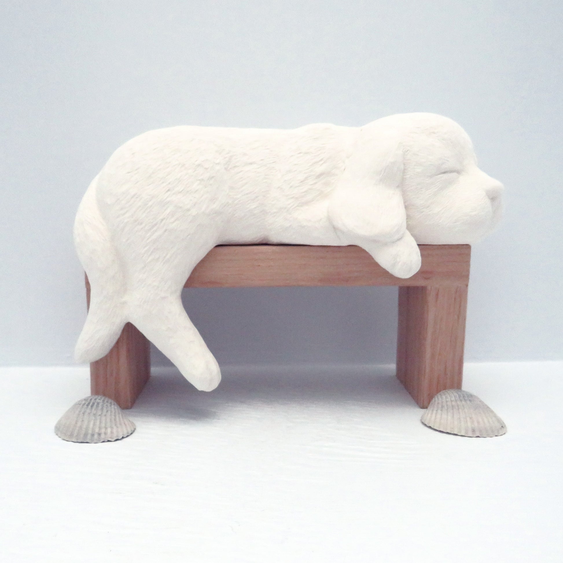 Ready to paint ceramic dog figurine on wood pedestal with sea shells on the pale blue table.  This is a side view of the dog