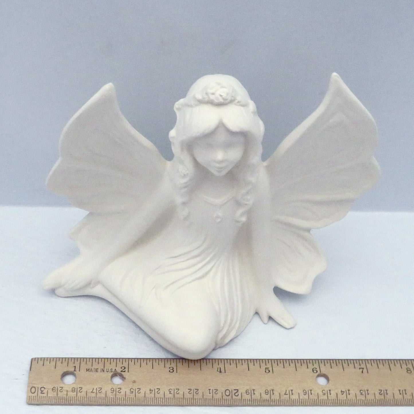handmade paintable ceramic fairy figurine from a higher view showing a ruler. She is approximately 7 inches wide