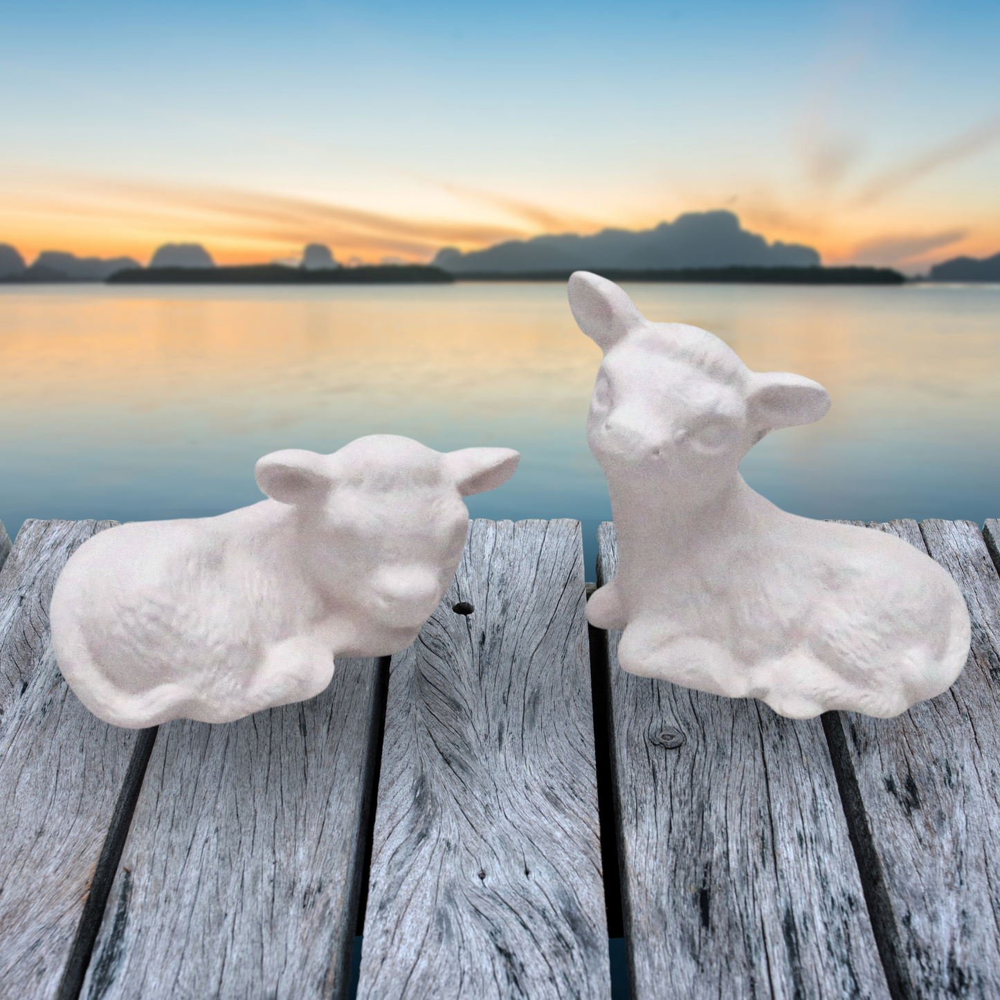 set of 2 ready to paint ceramic cows sitting on a rustic table by the ocean