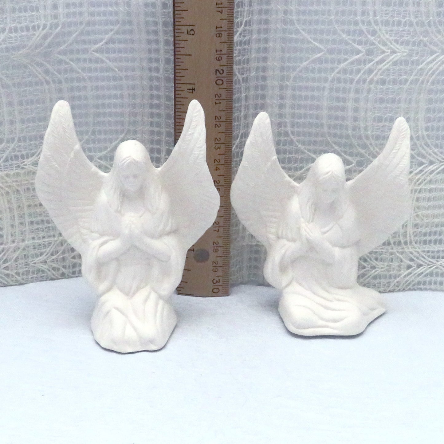 Handmade ceramic angels to paint in front of a ruler showing the tip of the wing to be almost 4 inches high. The sitting angel is a bit shorter.