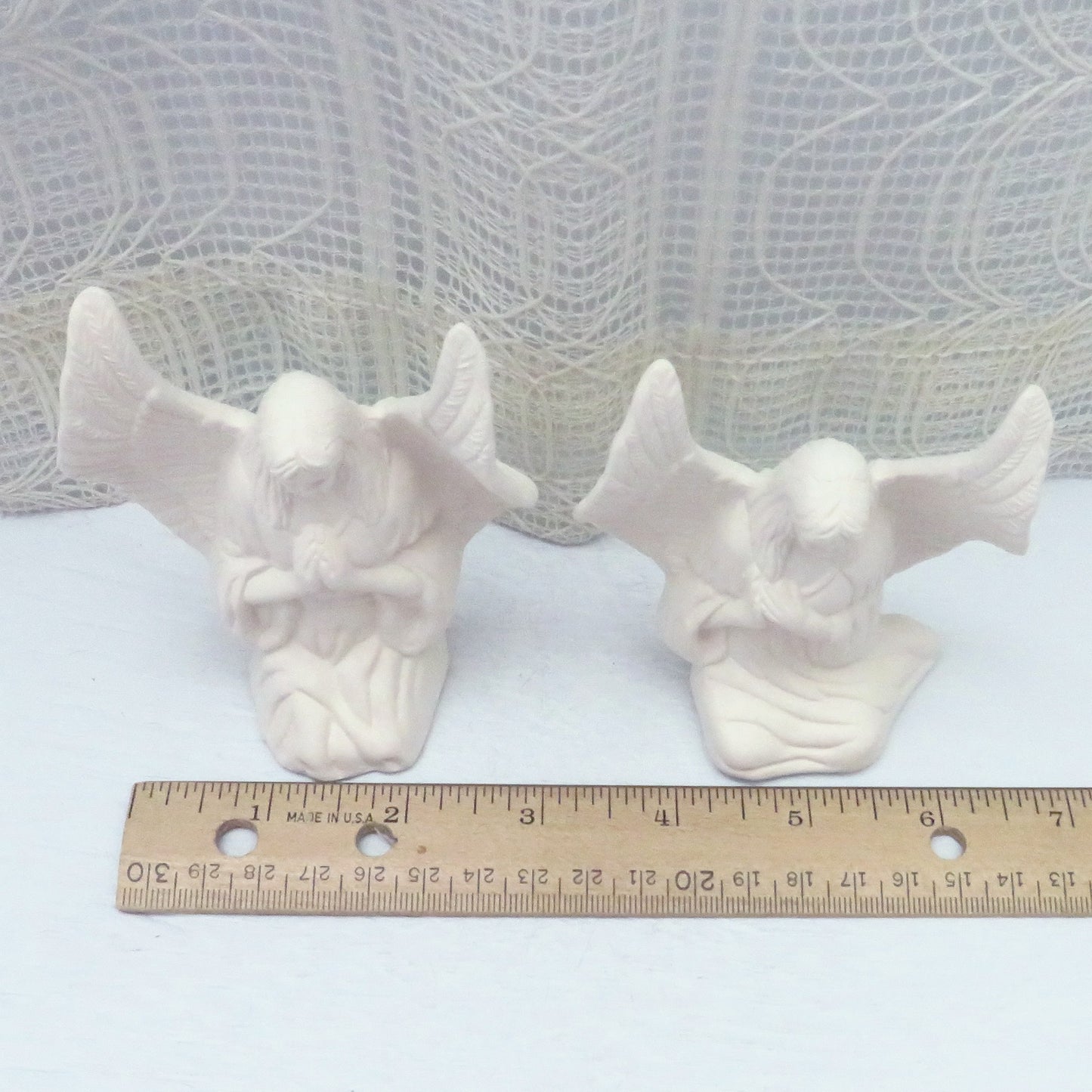 Handmade DIY ceramic angel figurines near a ruler showing them to be approximately 3 inches wide. This is a top view looking down.
