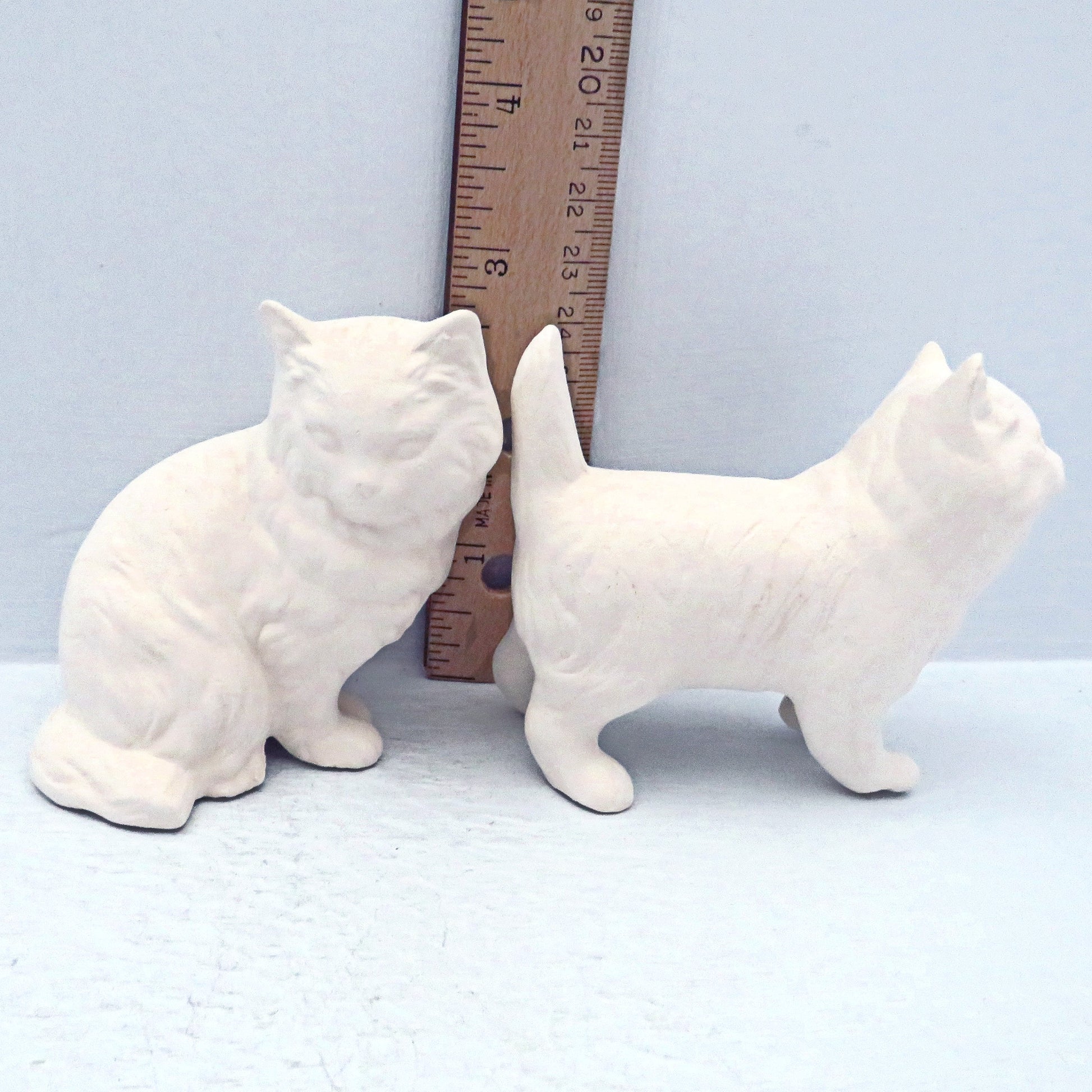 2 unpainted ceramic cat figurines near a ruler showing them to be approximately 2 3/4 to 3 inches tall