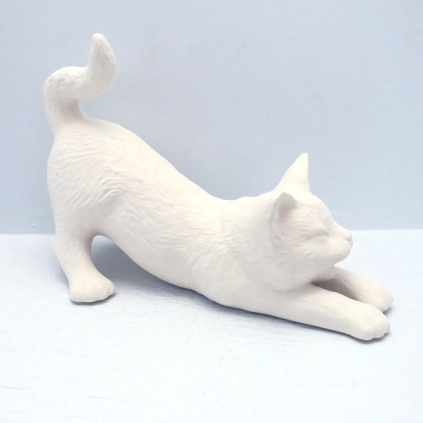 Handmade ready to paint ceramic stretching cat angled so its head is to the right. Its tale and rear end are up.
