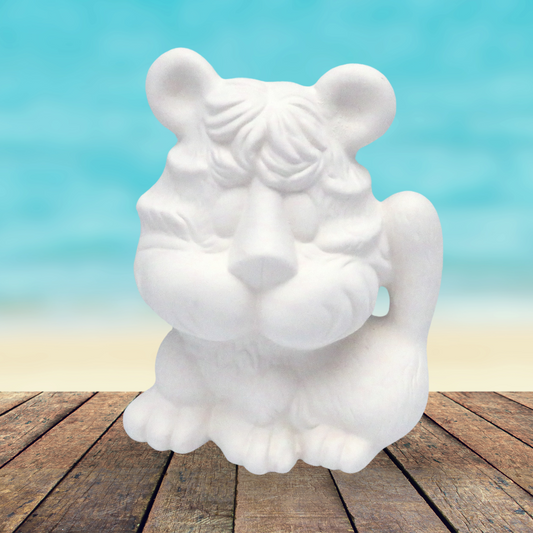 Ready to paint ceramic tiger figurine sitting on a rustic wooden table by the beach.