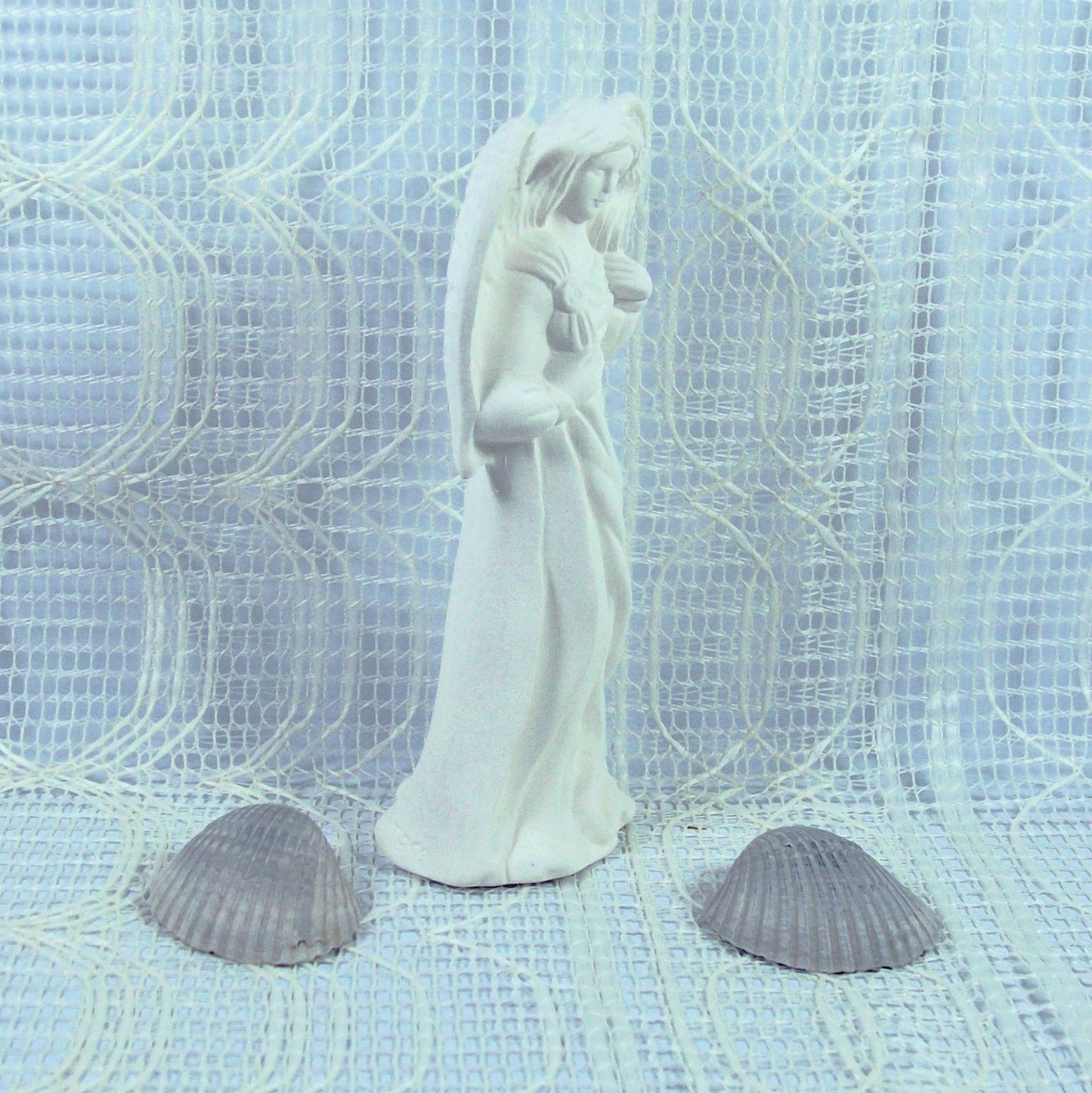 Side view of standing angel with wings tucked in.  She is standing on an ecru lacy table cloth.