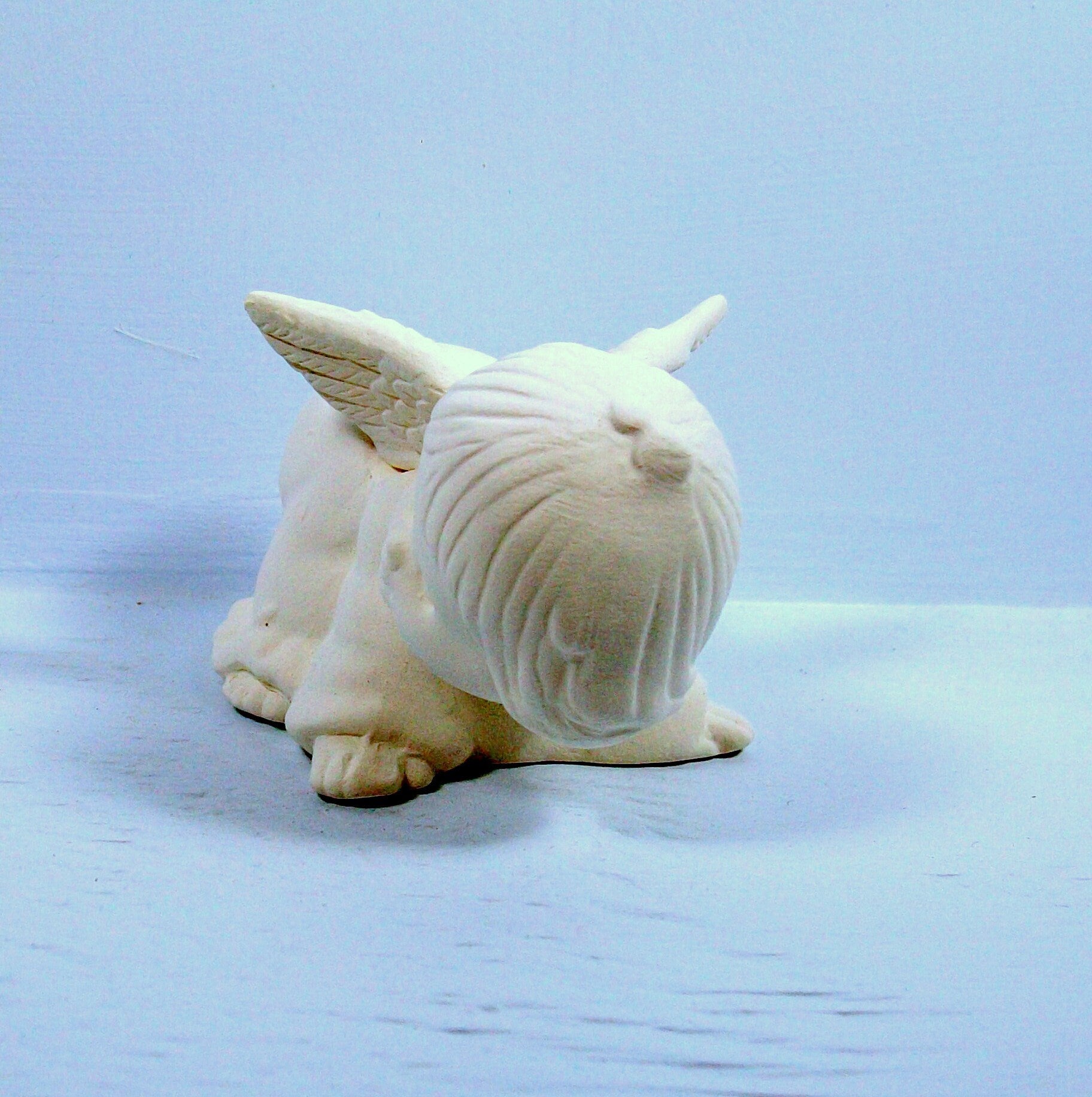 Handmade paintable ceramic angel statue on all 4's with head toward camera.