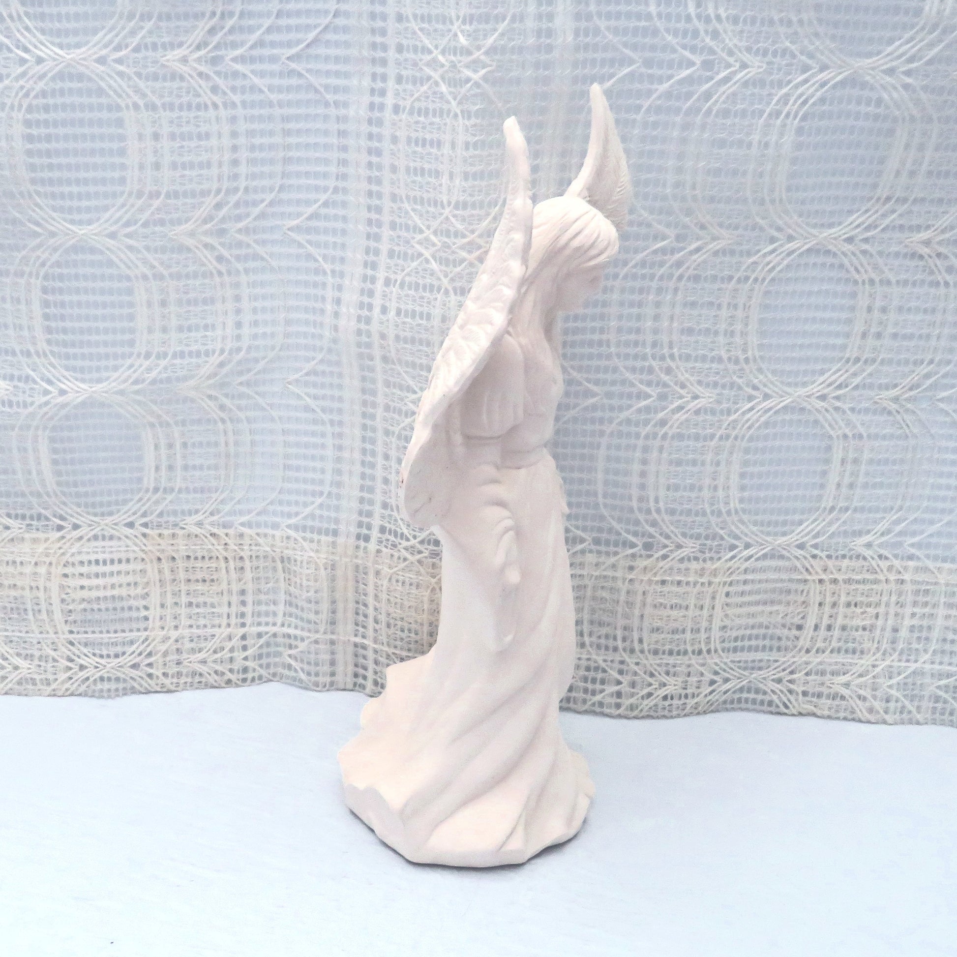 Side view of ready to paint ceramic angel figurine facing right.  This photo shows her wings and dress.