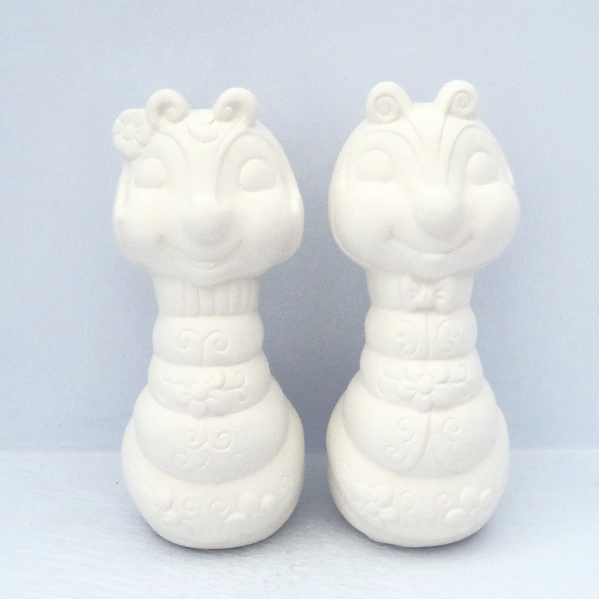2 handmade unpainted ceramic bug statues facing forward on pale blue background