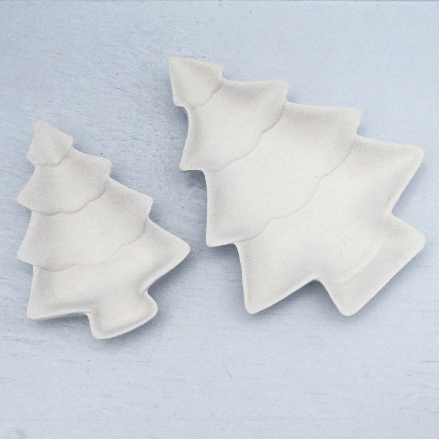 2 ready to paint Christmas tree trinket dishes on a pale blue background