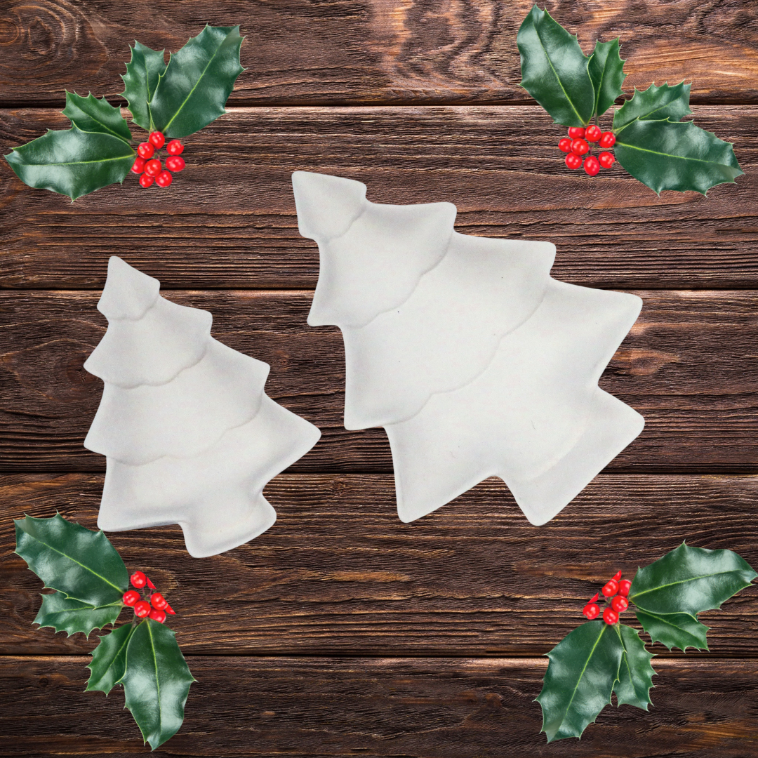 2 unpainted ceramic bisque Christmas tree shaped trinket dishes on a dark wood background with holly leaves and berries in the corners