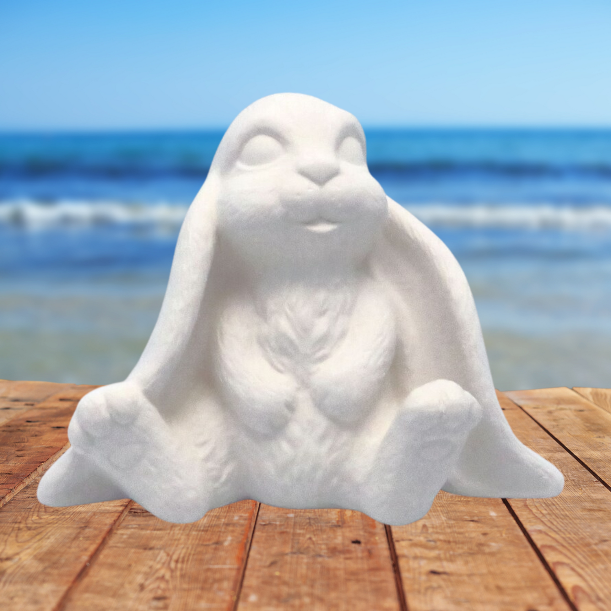 Handmade Ready to Paint Ceramic Lop Earred Bunny Figurine facing forward sitting on a table near the ocean
