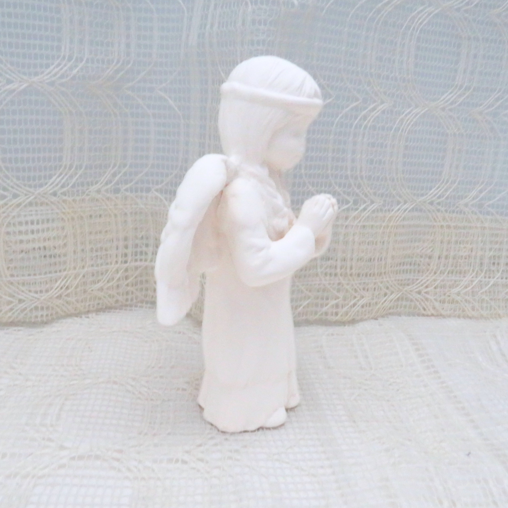 Side view of paintable ceramic angel statue on a lacy table cloth
