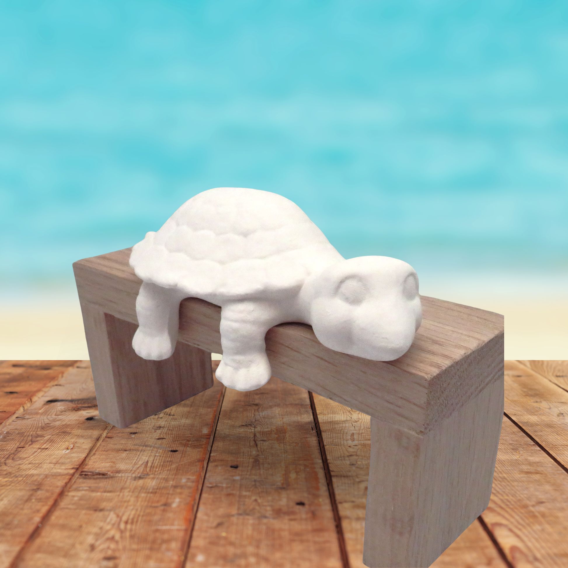 White ready to paint ceramic turtle on a wood shelf on a wooden table near the ocean.