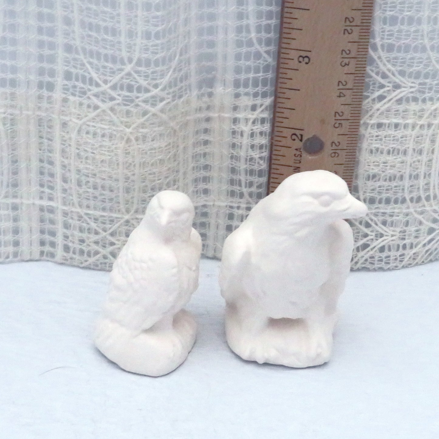 2 small ceramic bisqueware eagle figurines near a ruler showing the taller eagle to be approximately