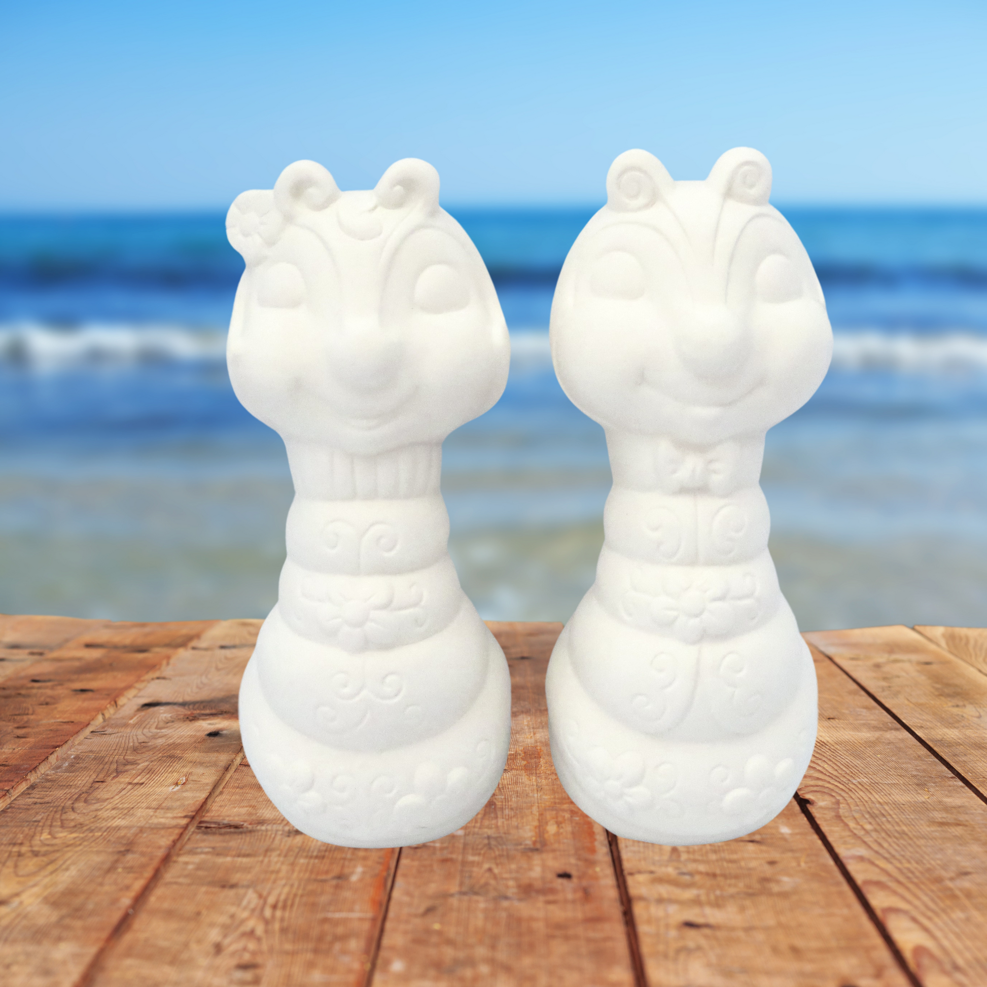 2 Ready to Paint Ceramic Bug figurines facing forward on a table by the ocean
