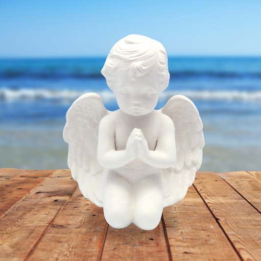 handmade kneeling ready to paint cherub with hands folded sitting on a wood table near the ocean.