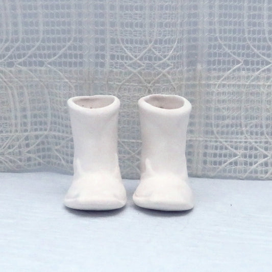 Set of 2 unpainted ceramic boots with holes in the back for Christmas tree ornaments.  They are toe forward on a bue table with an off white background