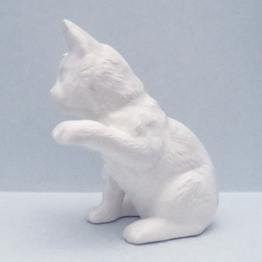 Handmade unpainted ceramic sitting cat facing left with front paw up
