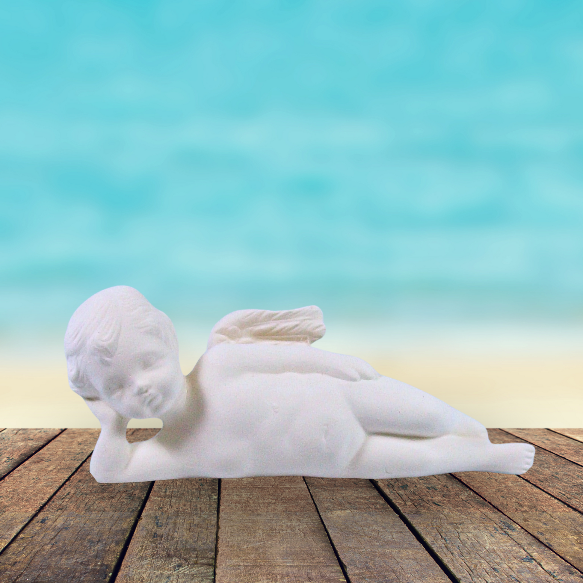 Unpainted cherub lying on side on a rustic table by the ocean.