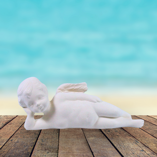 Unpainted cherub lying on side on a rustic table by the ocean.