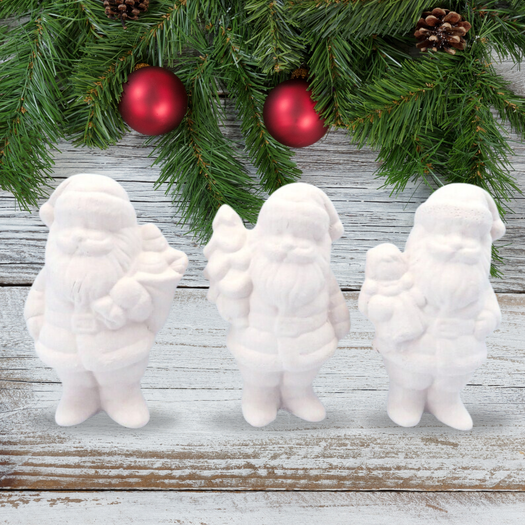 3 ready to paint ceramic santa claus figurines on a rustic wood background with pine branches, red ornaments, and pine cones.