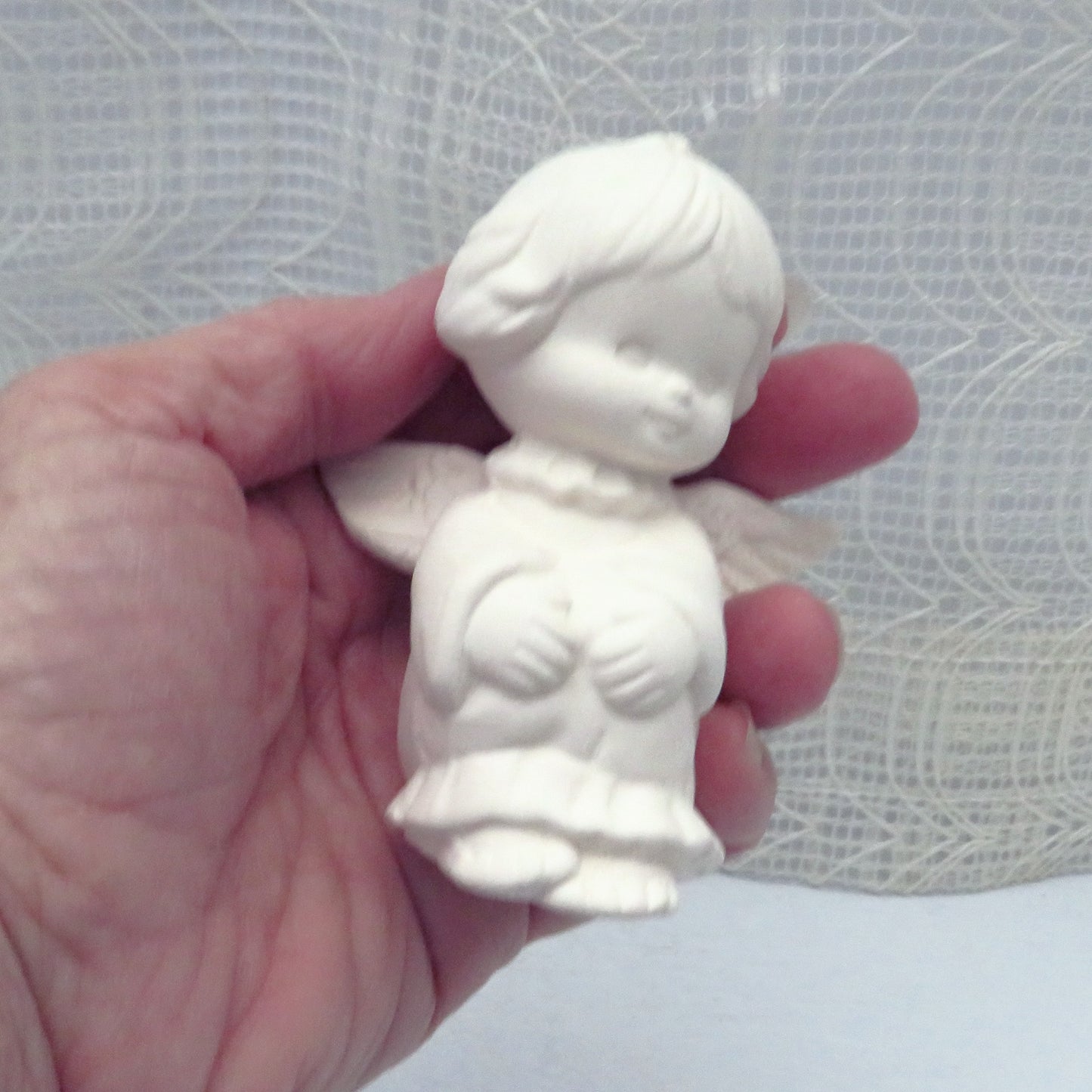 Unpainted bisque ceramic angel in my hand showing a size comparison.