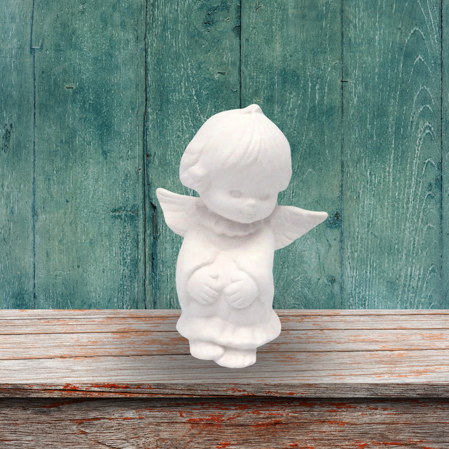 Handmade paintable ceramic angel sitting on a rustic shelf with distressed green background