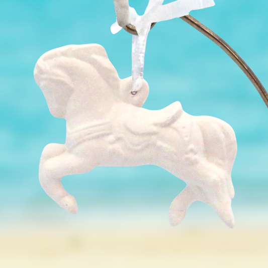 White unpainted ceramic carousel horse on an aqua background hanging on a metal hanger.