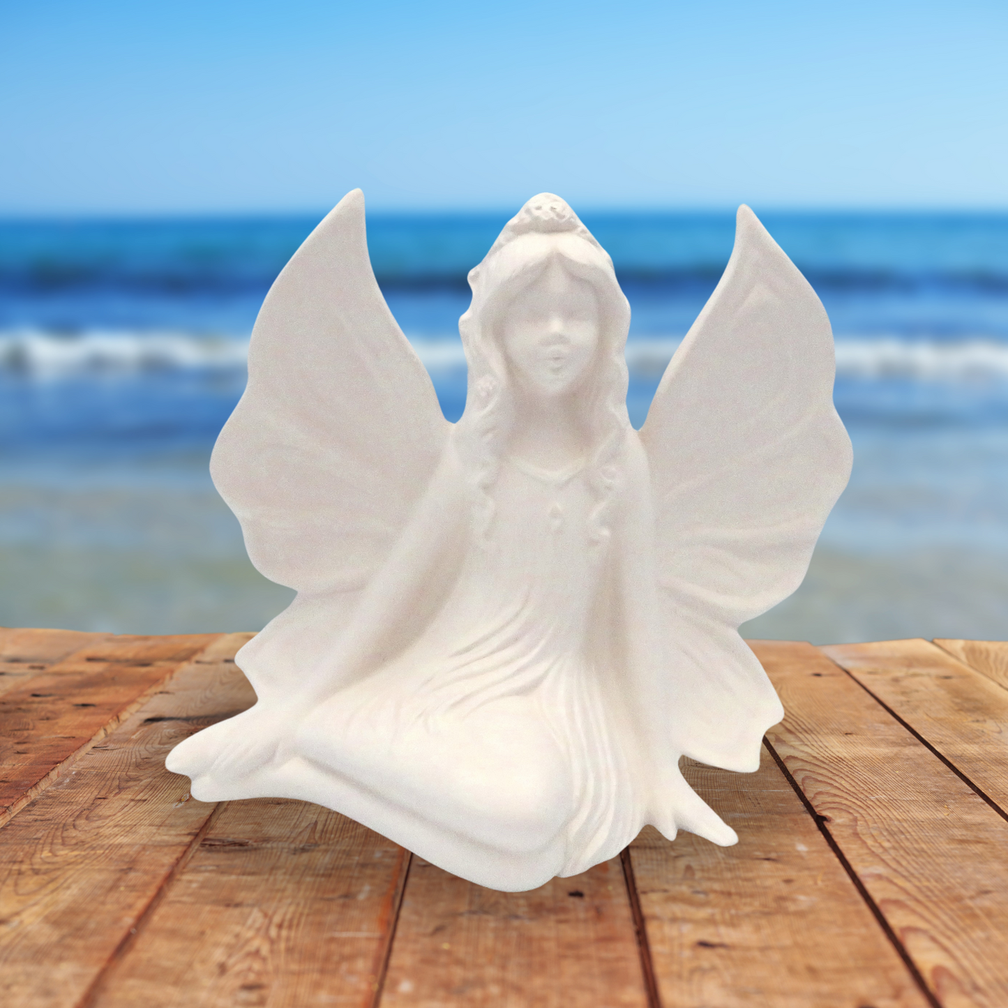 Handmade ready to paint side sitting fairy on a wooden table by the ocean