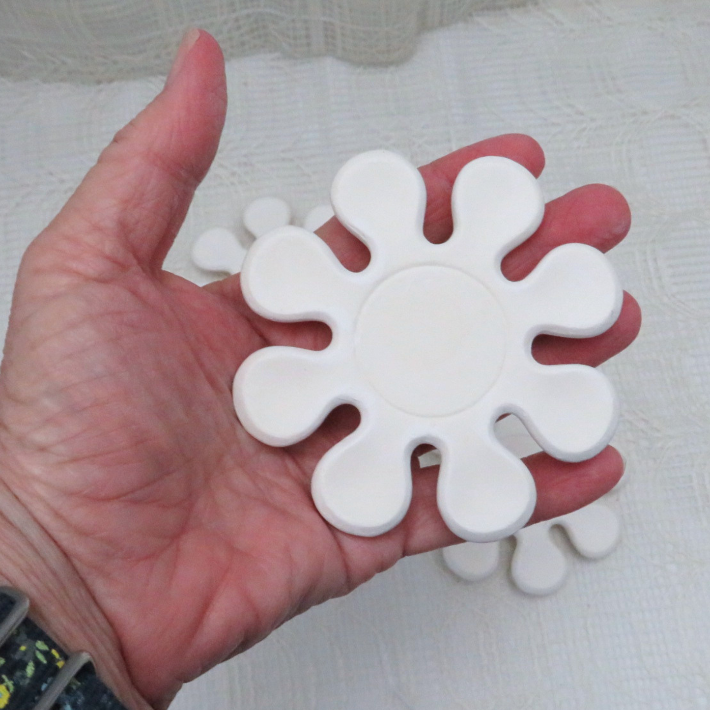 Handmade flower shaped ceramic coaster for a paint project in my hand to illustrate size.