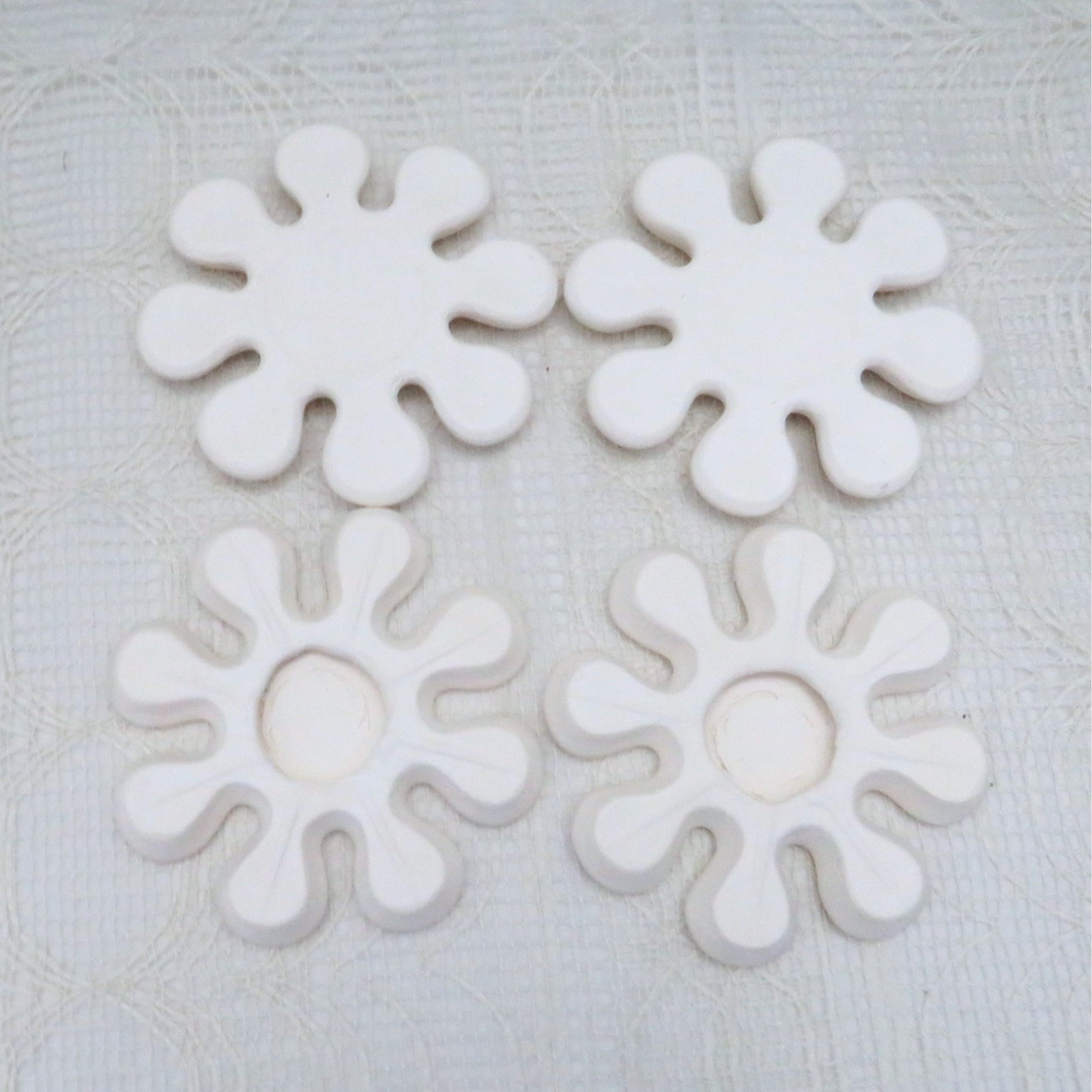 handmade ceramic flower shaped coasters on a lacy table cloth.  2 of them are showing the front side and 2 show the back side.