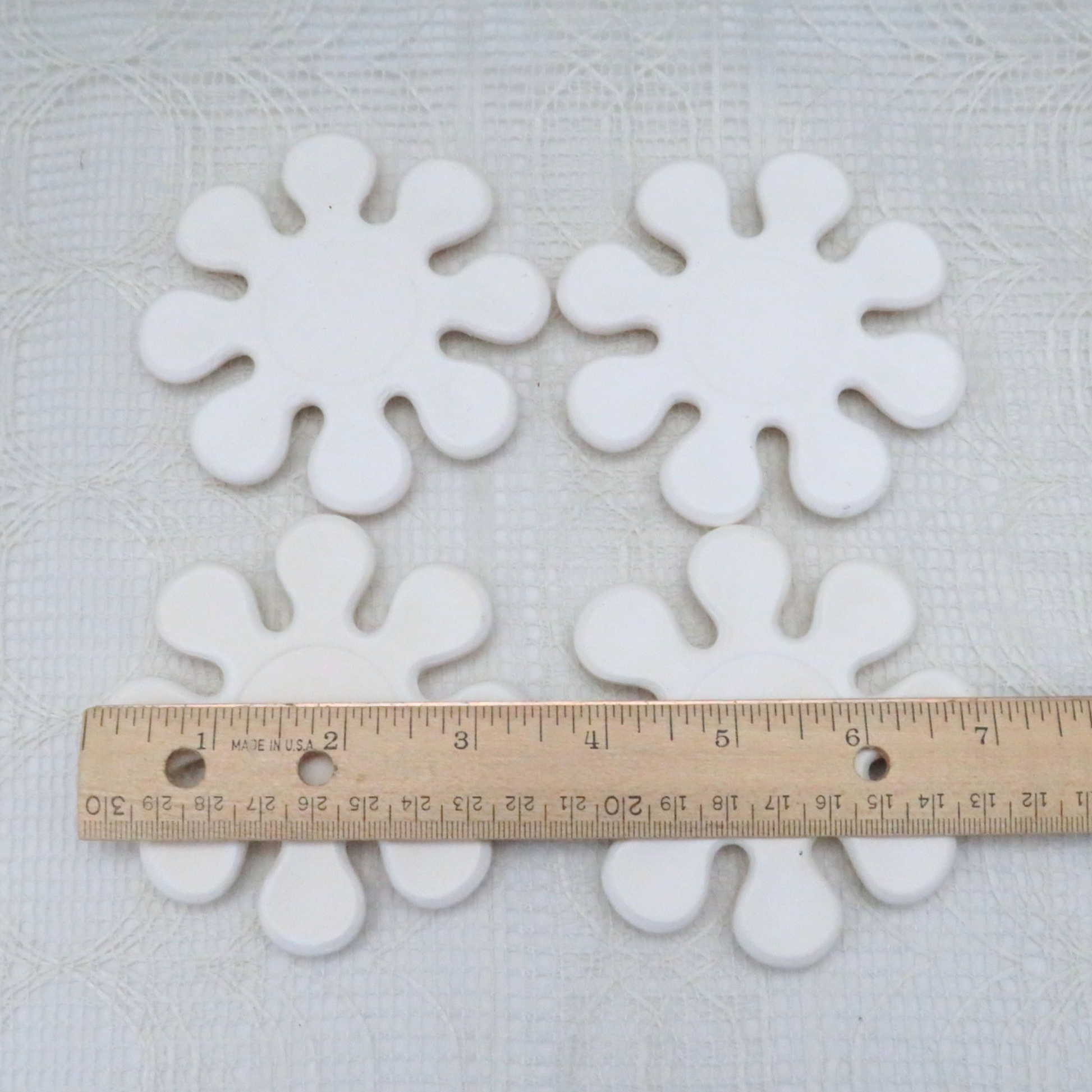 Set of 4 paintable ceramic bisque flower shaped coasters with a ruler to illustrate size.