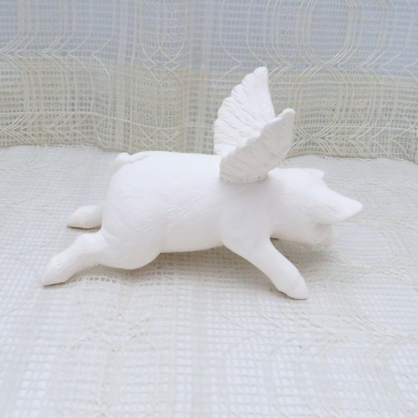 Handmade paintable ceramic pig angel with wings outstretched in the flying position facing right.