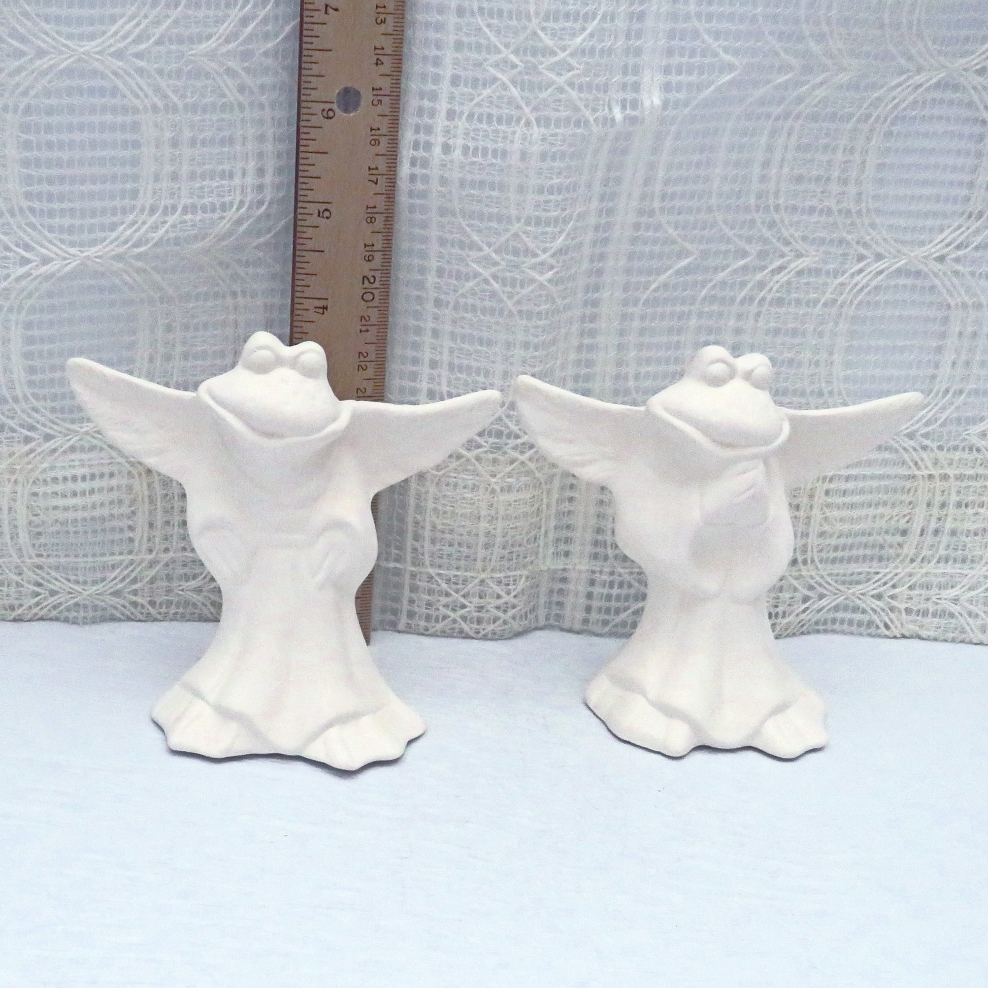 2 ready to paint ceramic frog angel figurines in front of the ruler showing them to be almost 4 inches tall