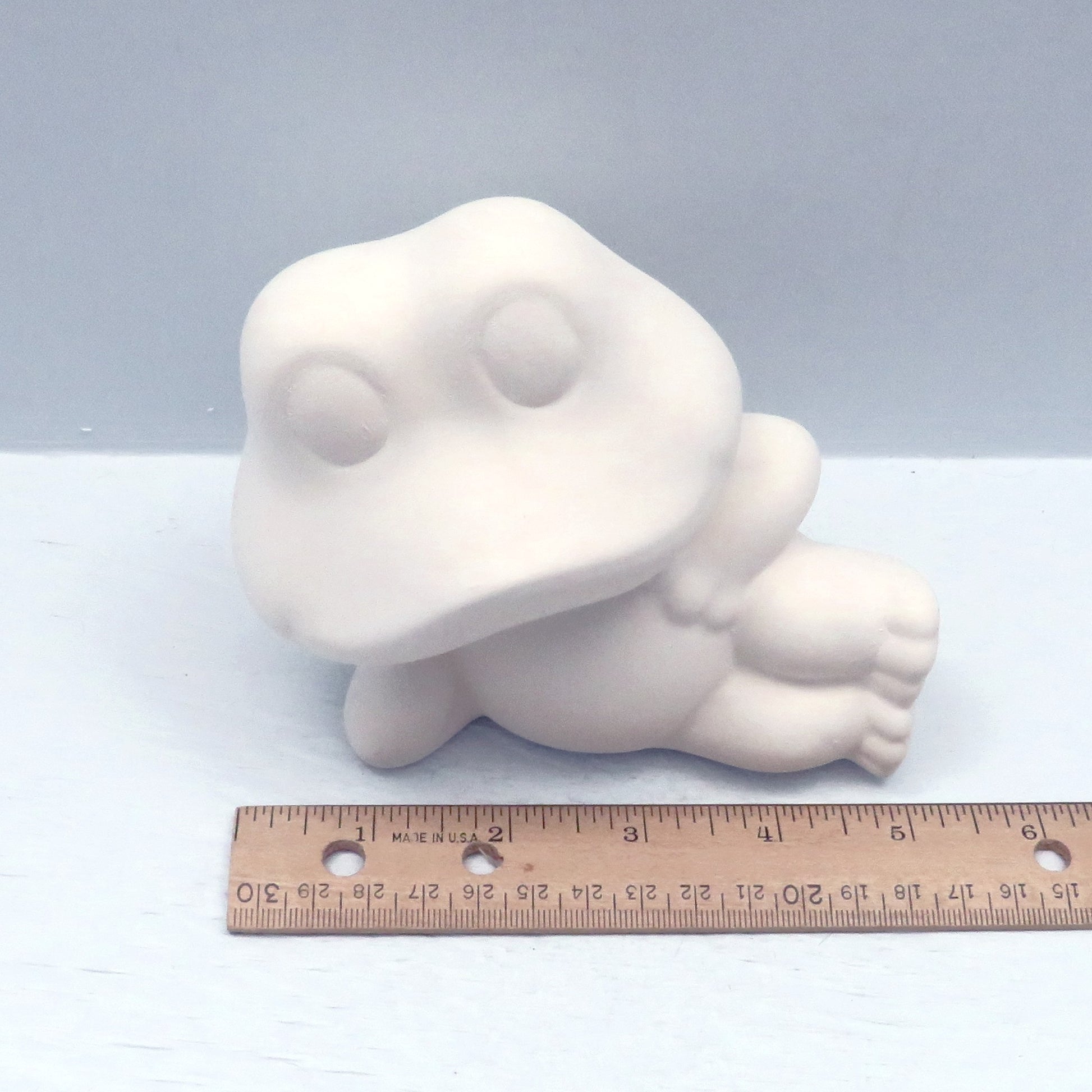 handmade paintable frog statue lying on side near a ruler showing it to be approximately 5 inches long.