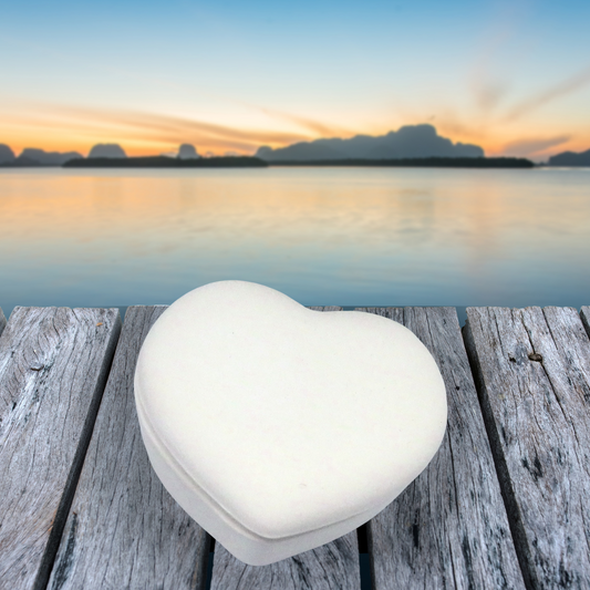 Unpainted ceramic heart lidded dish on a wooden table by the ocean.