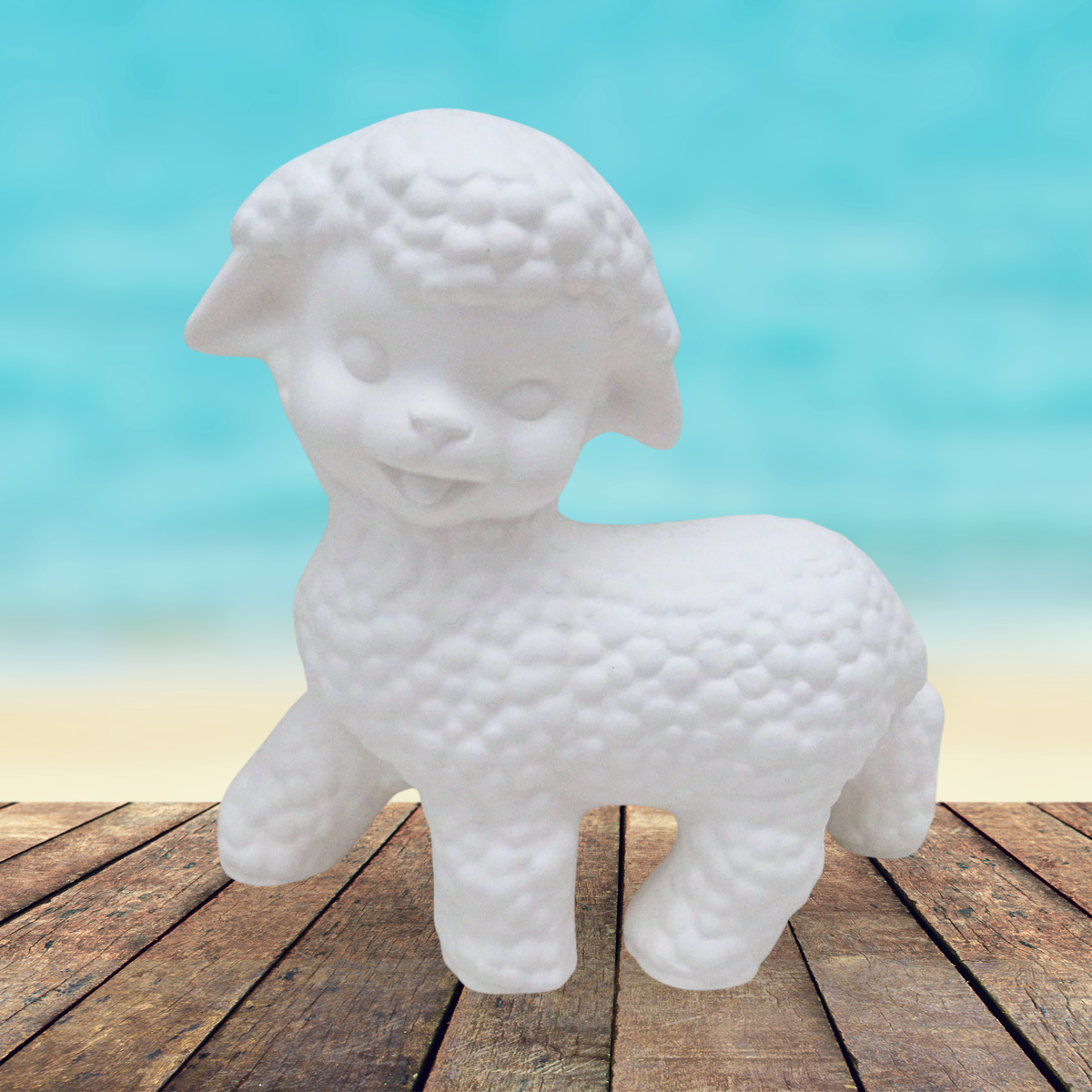 Handmade ready to paint ceramic lamb on a rustic wooden table by the ocean 