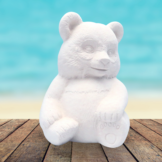 handmade ready to paint ceramic panda figurine sitting on a rustic table by the beach and ocean